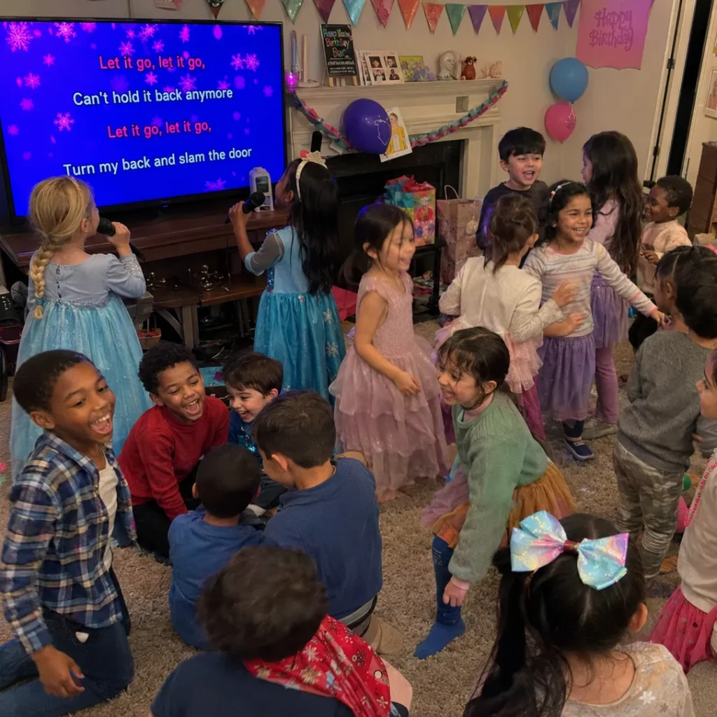 Lots of children in the living room celebrating a birthday party with karaoke.